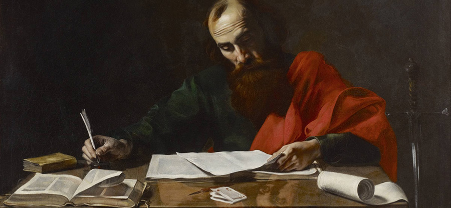The Apostle Paul sitting at a table, writing on parchment with scrolls and books laid out in front of him.